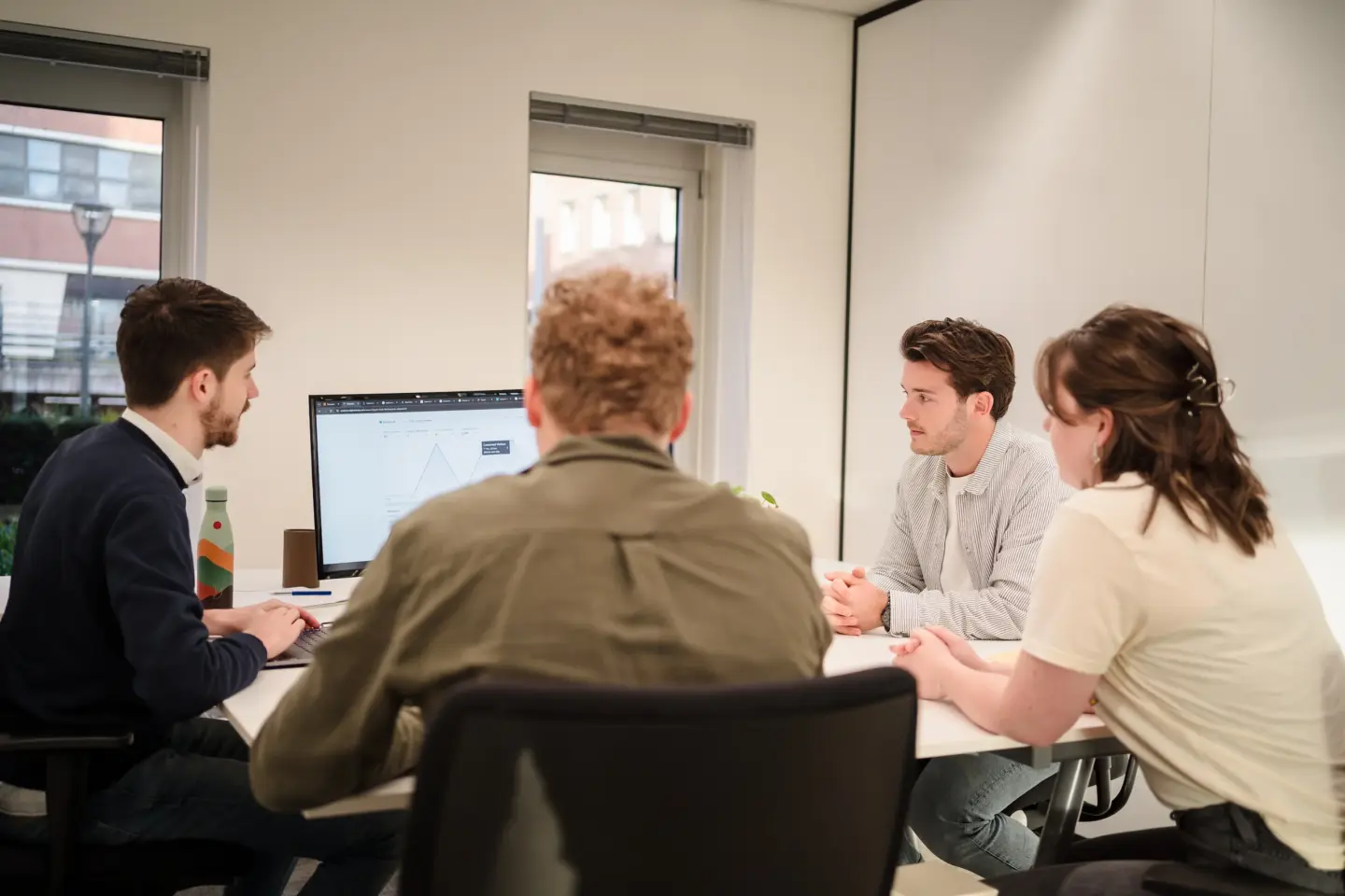 Overleg aan tafel met klant, documenten en laptop, serieus maar ontspannen